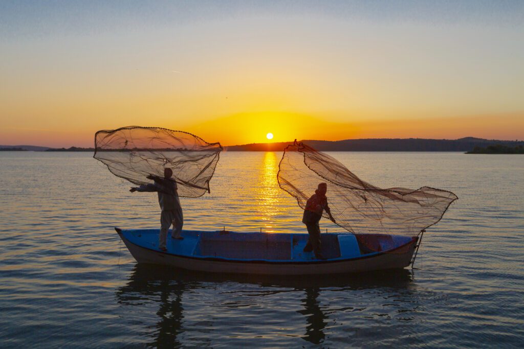 Two man in the boat releasing their fishing nets to the sea