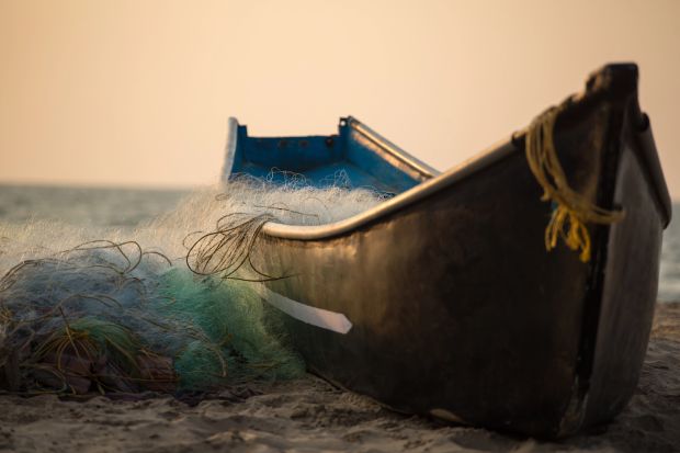 A boat resting on the beach beside a fishing net